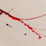 Línea de tinta roja con salpicaduras azules en detalle de la obra "Descosido", sobre papel artístico.